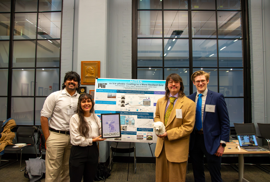 Four MIT students pose in front of a research poster titled "MITTEN: An Ice-Phobic Coating for a More Resilient Grid" at the MADMEC competition, with one team member holding a small polar bear figurine and another displaying a tablet.
