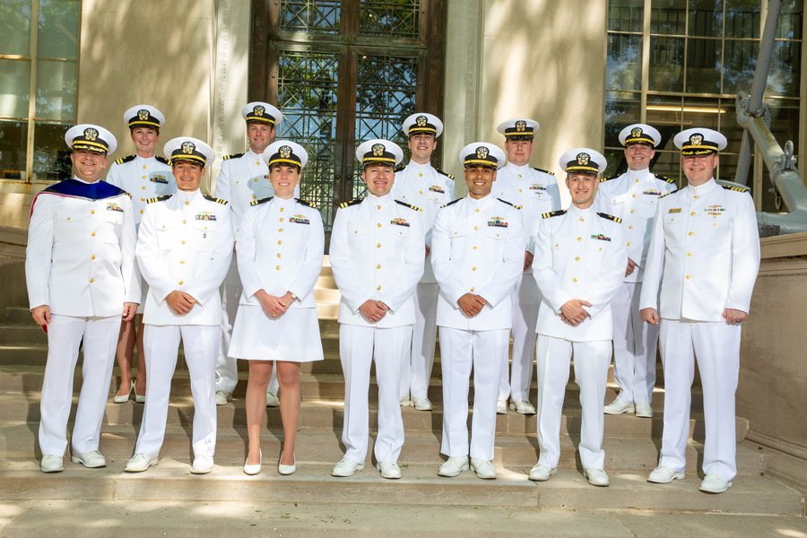 A group of people in white dress uniforms posed on outdoor steps in front of a building.