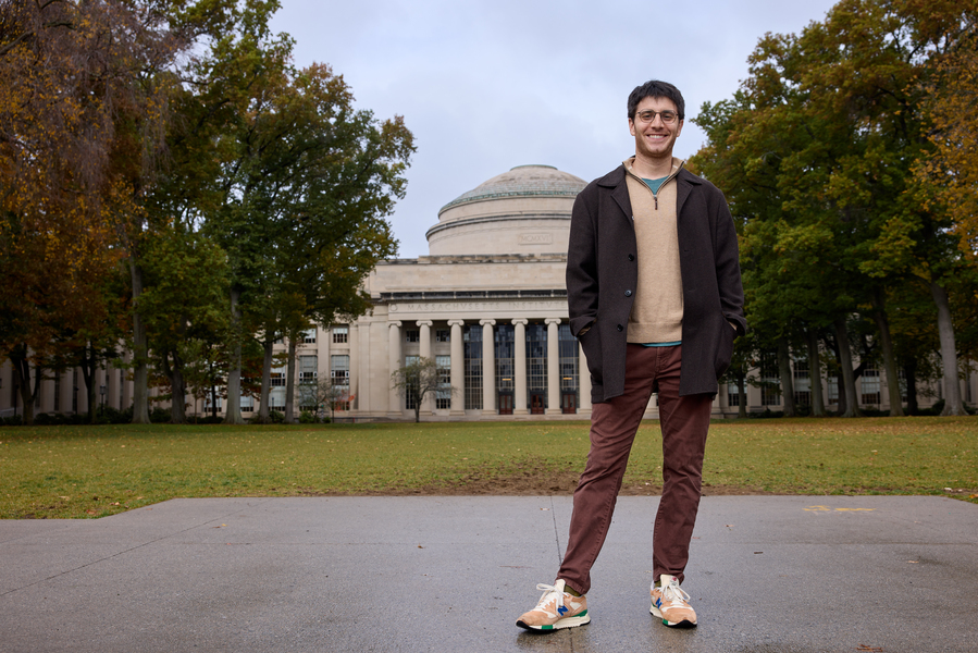 A person stands on a walkway in front of MIT’s Great Dome, surrounded by trees and an open lawn.
