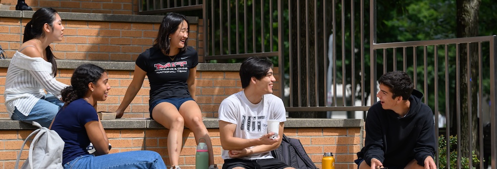 A group of five students sitting on outdoor steps, engaged in conversation.