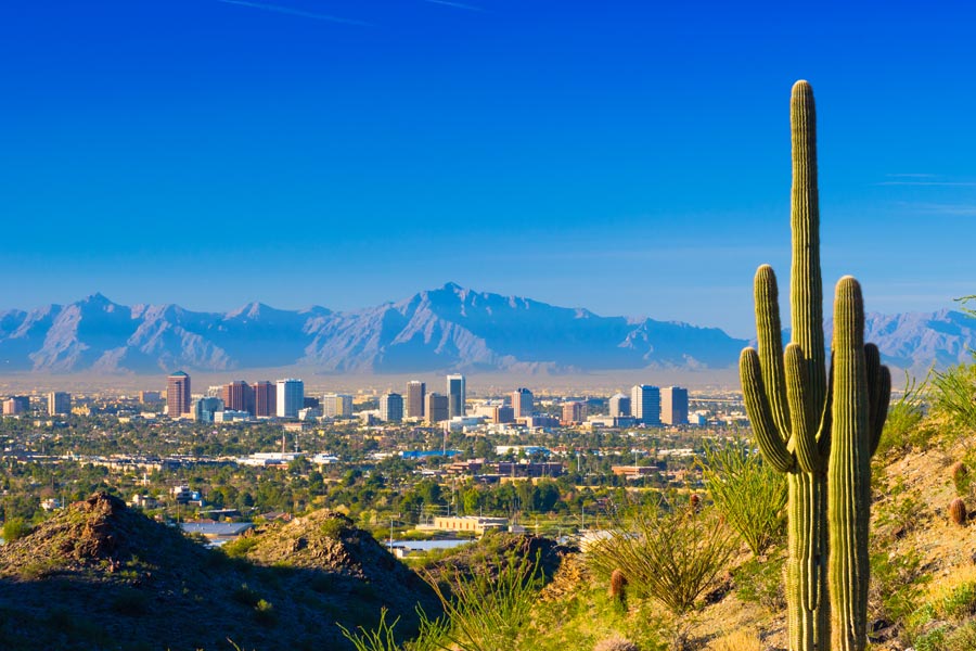 Phoenix, Arizona skyline viewed from a desert hillside with a saguaro cactus in the foreground and the Four Peaks mountain range in the background.