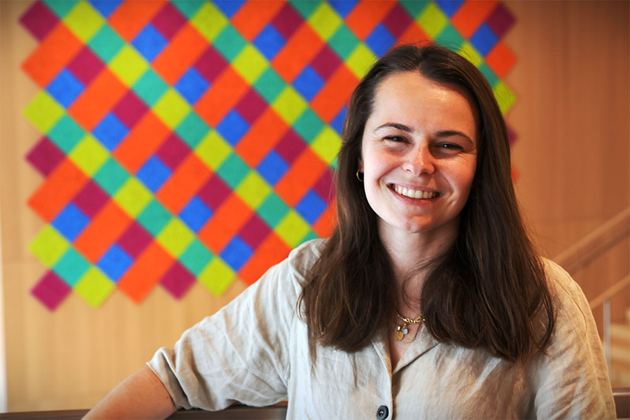 A woman smiles at the camera in front of a colorful diamond-patterned wall hanging.