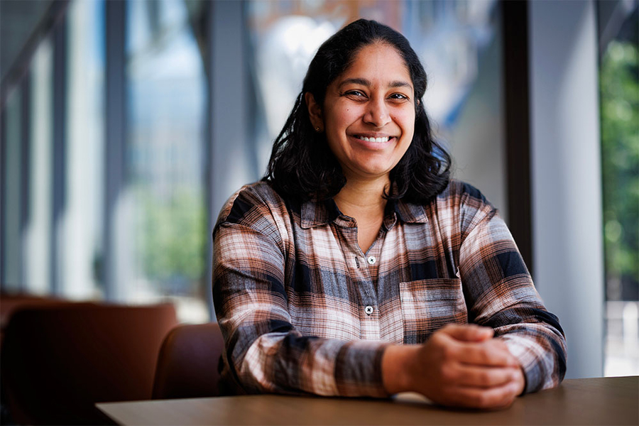 A smiling woman with brown hair sitting behind a table with her hands clasped.