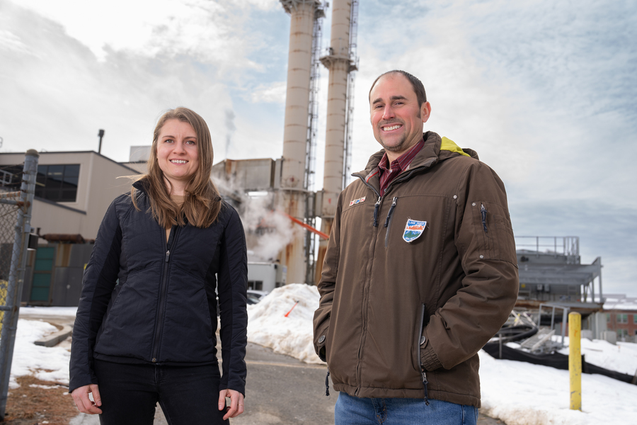 Jean Sack and Chris Lashway pose outside on a winter day, with a power plant in the background.