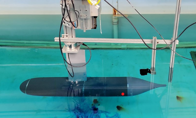 Laboratory setup testing a streamlined underwater model in a clear water tank.