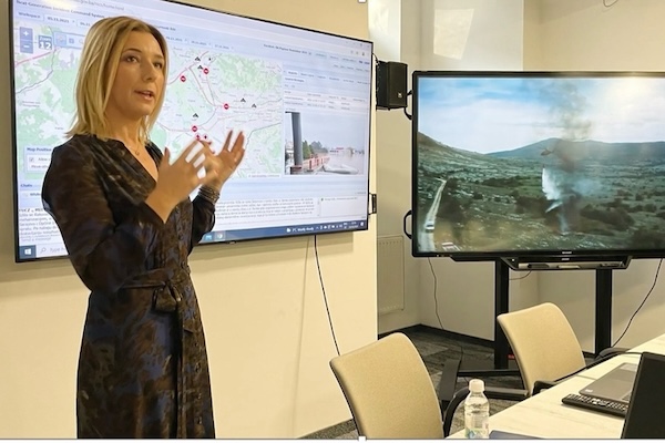 Mirnesa Softić speaks in front of two screens displaying a map and wildfire.