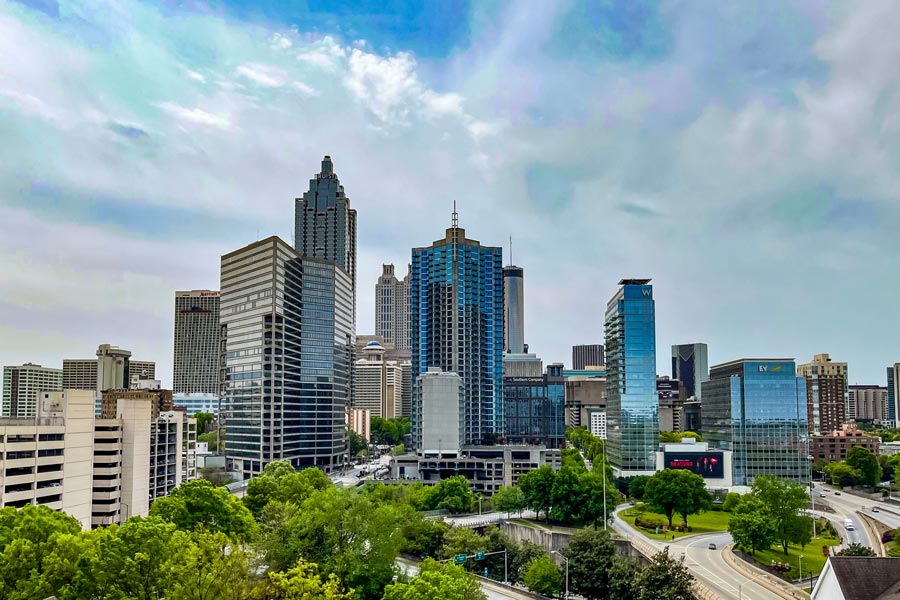 Atlanta, Georgia skyline rising above a canopy of spring trees, with the Truist Plaza and W Hotel tower prominent against a partly cloudy sky.