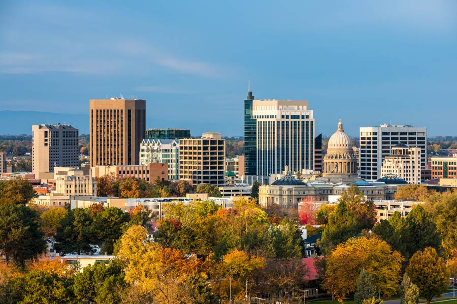 Boise, Idaho skyline in fall foliage, with the Idaho State Capitol dome visible among downtown skyscrapers against a blue sky.