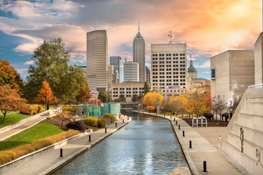 Indianapolis, Indiana skyline in peak fall foliage, viewed along the Central Canal Towpath with the Indiana State Capitol dome visible at right.
