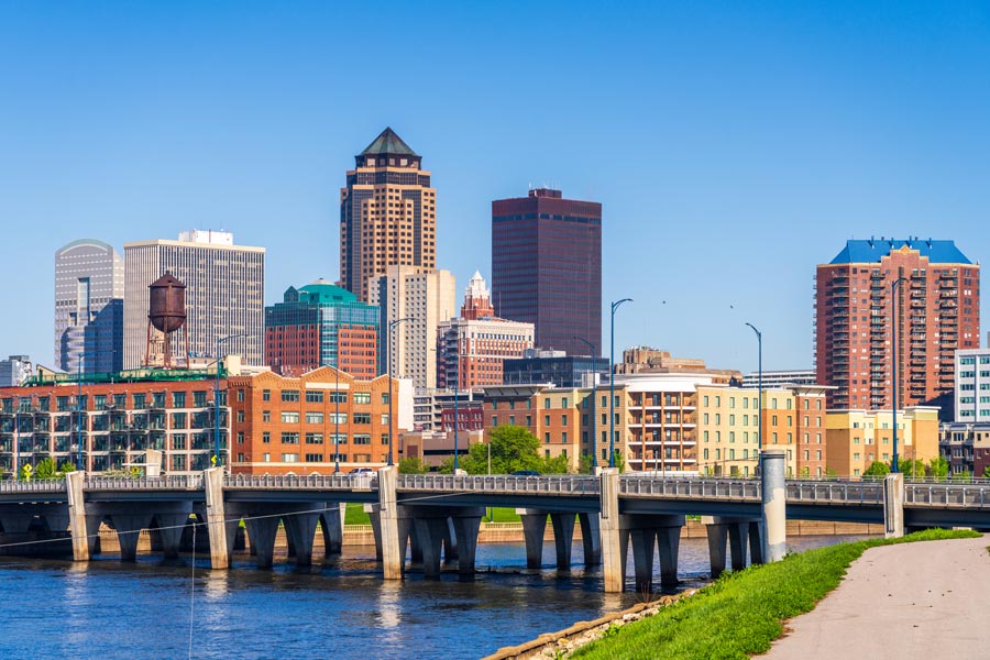 Des Moines, Iowa skyline viewed from the Des Moines River, with a bridge in the foreground on a clear, sunny day.