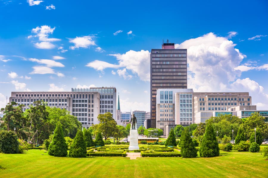 View from the Louisiana State Capitol grounds in Baton Rouge, with a bronze statue amid formal gardens and government buildings stretching to the horizon.