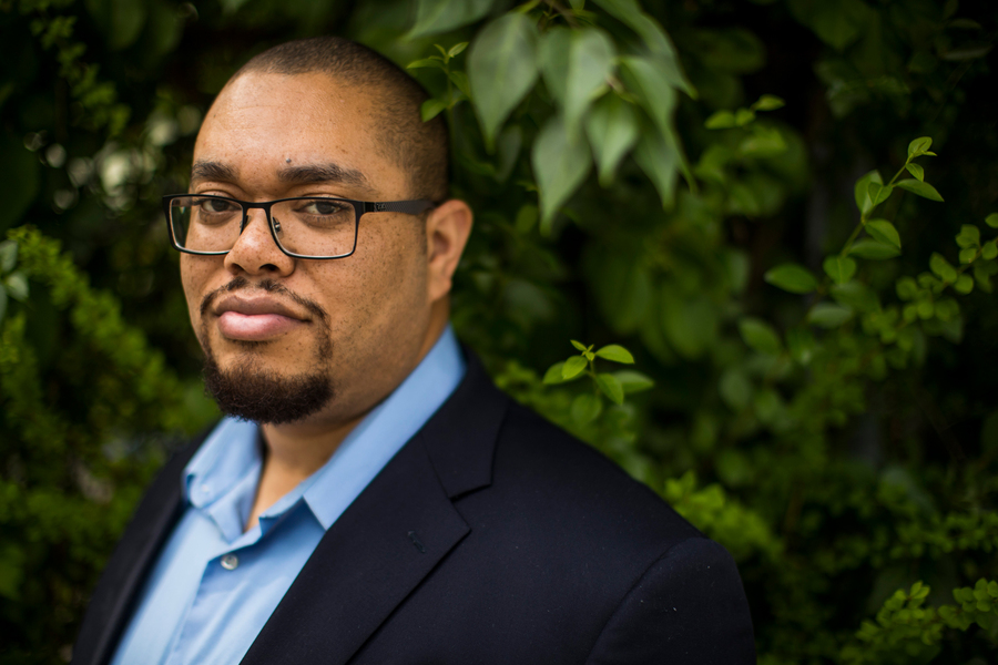 An MIT professor wearing glasses and a blue shirt, photographed outdoors against a lush green leafy background.