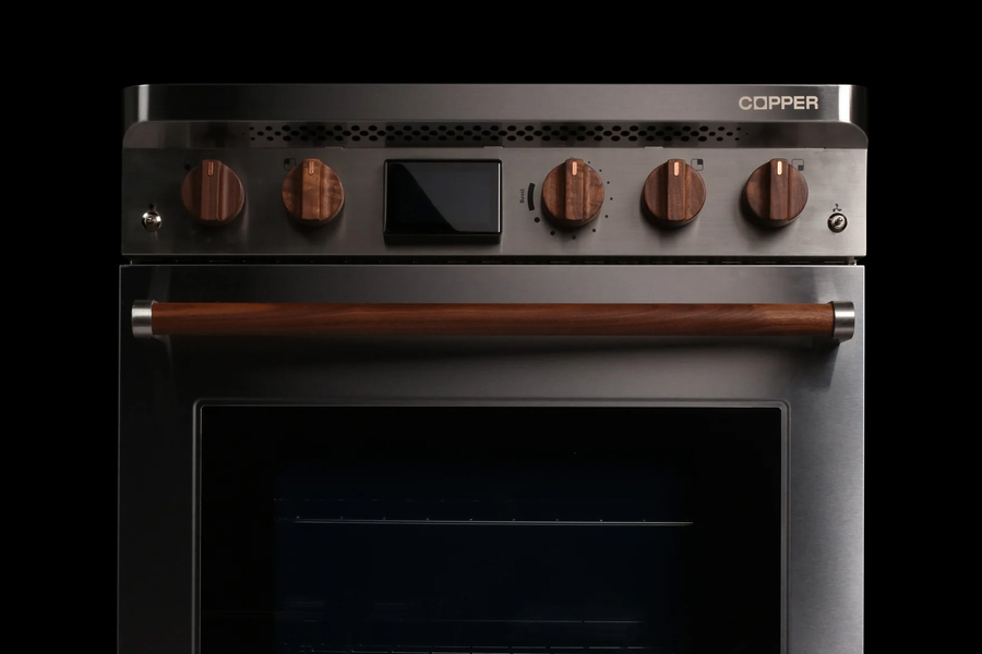 A modern stainless steel oven with a sleek design, featuring four round wooden control knobs, a central digital display, and a horizontal wooden handle on the oven door. The brand name “Copper” is visible on the top right corner of the control panel.