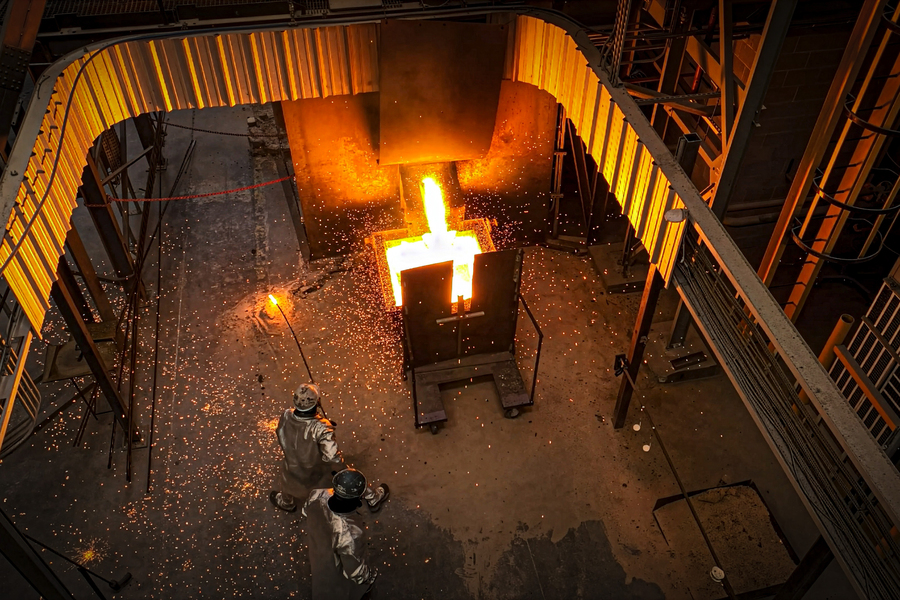 Molten metal being poured in an industrial foundry, viewed from above with glowing sparks.