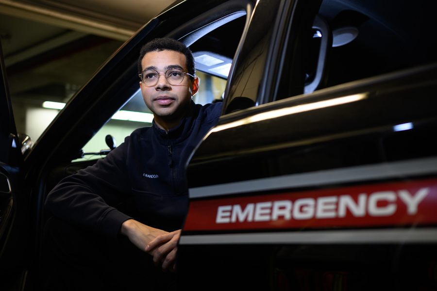 A man in glasses sits in the driver's seat of a vehicle marked "Emergency."