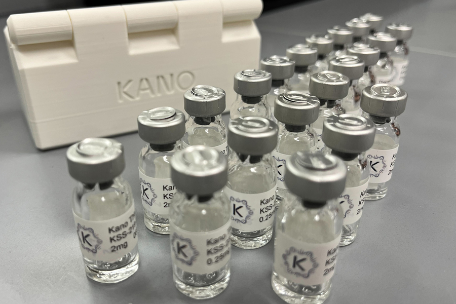 Multiple small glass vials with labeled caps arranged in rows beside a white container marked “Kano"