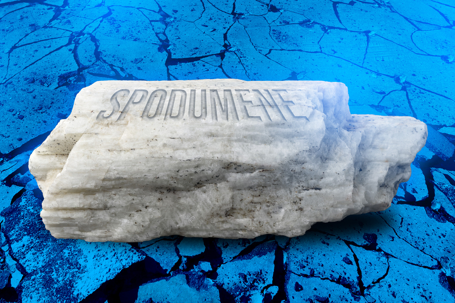 A white chunk of rock with the word "SPODUMENE" carved into it, resting on a bright, cracked blue surface.