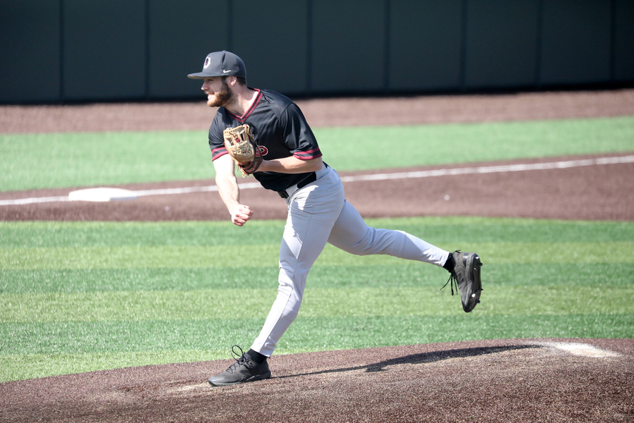 Player in dark uniform and cap executing a fielding position on baseball field during game.