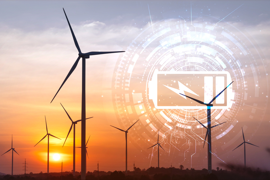 Wind turbines silhouetted against an orange sunset sky with a glowing digital overlay of a battery charging icon and circuit board design, representing renewable energy storage and thermal grid technology.