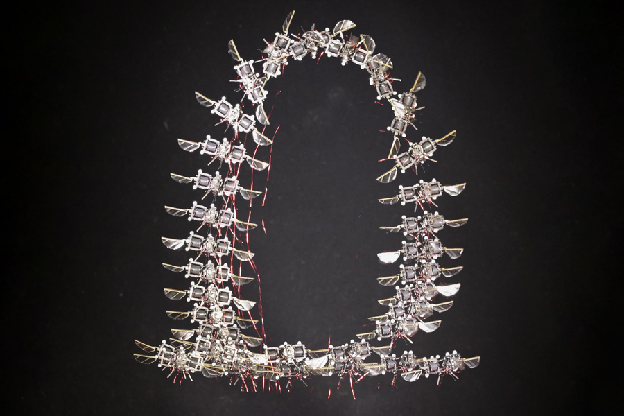 A ring-shaped formation of tiny metallic insect‑like micro‑robots arranged against a dark background.