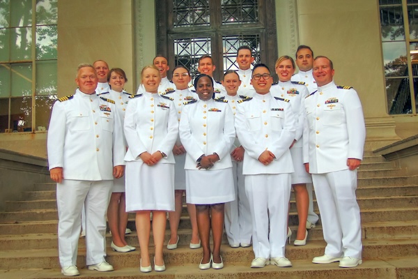 Fourteen graduates wear white navy uniforms on the steps of MIT's Building 5.