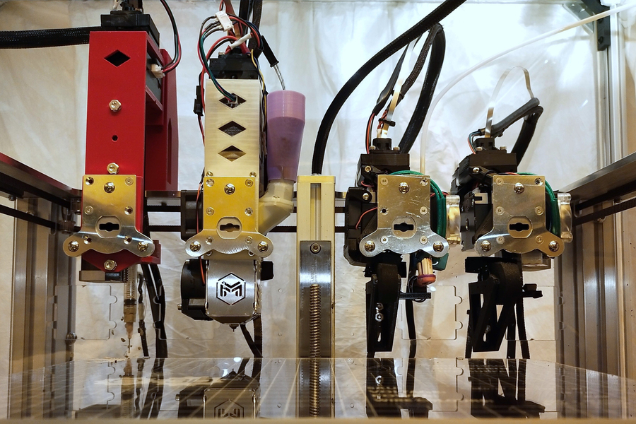 Close-up of multiple robotic tool heads aligned on a metal 3D printing machine.