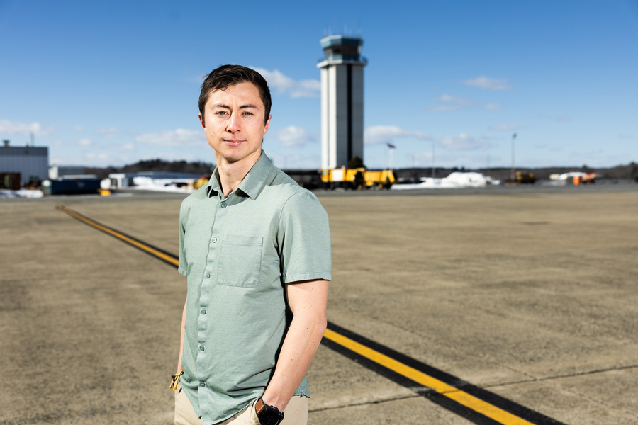 Person standing on an airport tarmac with a control tower in the background under a clear sky.