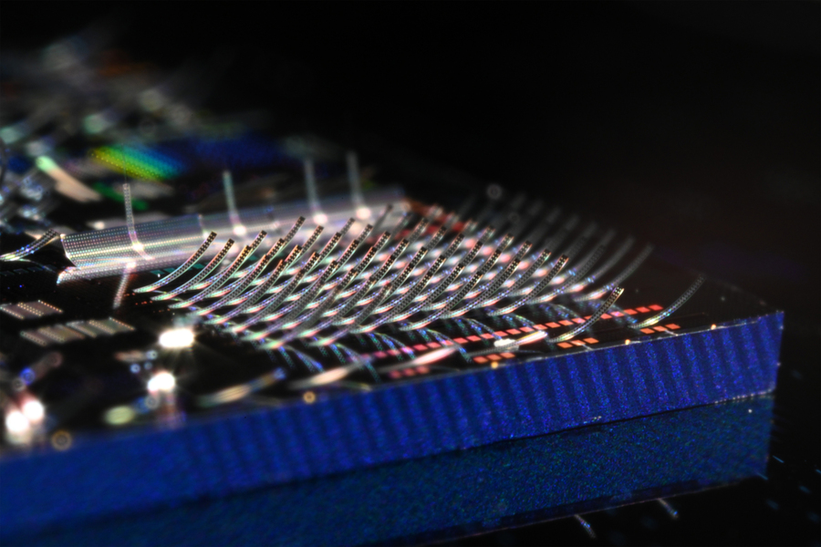 Close-up of fine wire bonds arching over a microchip on a dark circuit board.