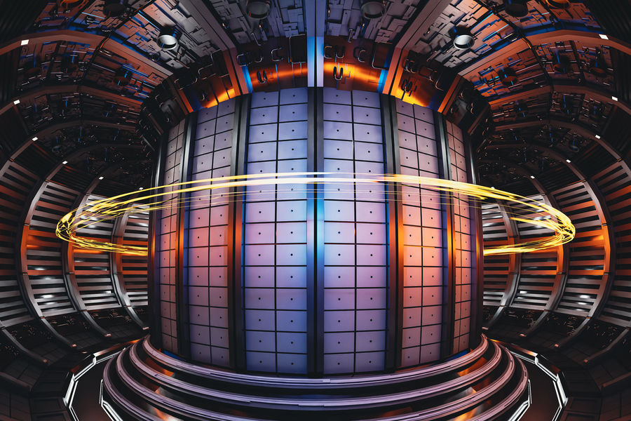 Interior view of a futuristic tokamak fusion reactor chamber with a large cylindrical core surrounded by metallic panels. Bright orange and blue lighting highlights the structure, and a glowing yellow ring of light encircles the core, suggesting plasma or energy flow.