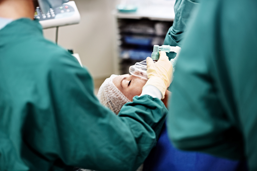 Medical staff administer anesthesia to a patient using a breathing mask in a surgical setting.