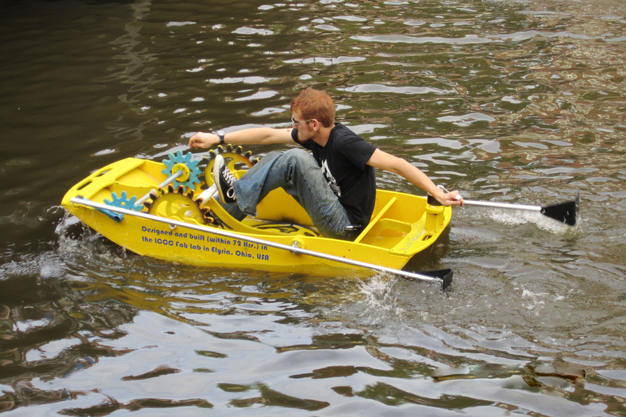 A student piloting a small bright yellow boat with visible gear mechanisms on a canal.