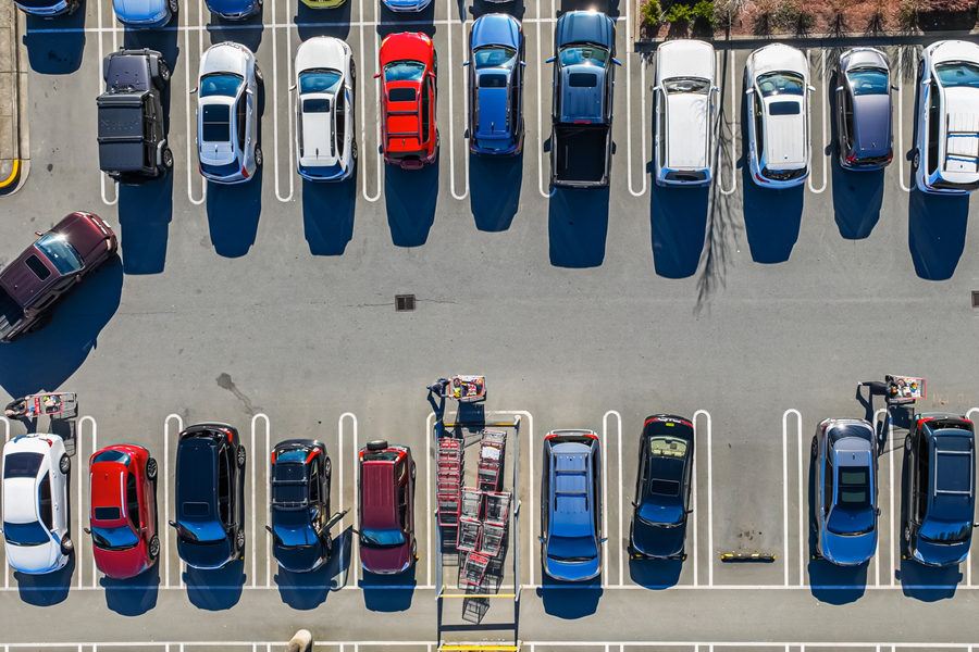 Aerial view of a parking lot with rows of cars and a shopping cart return in the center.
