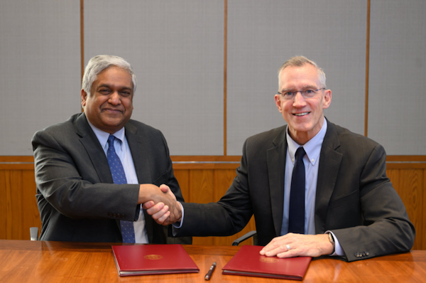 Anantha Chandrakasan and Gregg Bartlett, both in suits, sit at a table and shake hands for the camera.