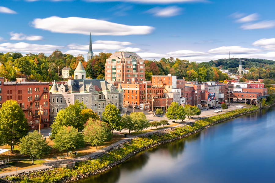 Augusta, Maine waterfront along the Kennebec River in early fall, with historic stone and brick buildings including a Victorian courthouse with a green copper turret.