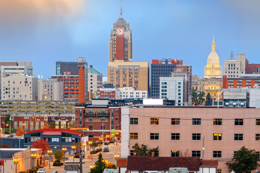 Downtown Lansing, Michigan skyline at dusk featuring a prominent clock tower and the illuminated Michigan State Capitol dome.