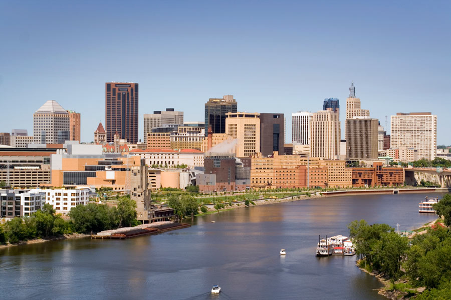 St. Paul, Minnesota skyline along the Mississippi River on a clear summer day, with a paddlewheel riverboat docked in the foreground.