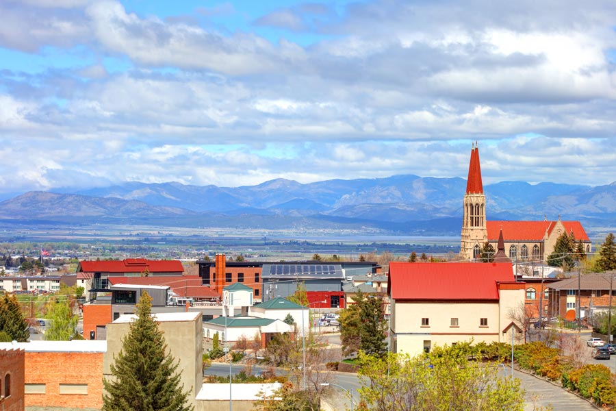 Downtown Helena, Montana with a Gothic-style cathedral, red-roofed buildings, and the Rocky Mountains stretching across the horizon.