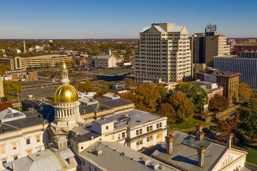 Aerial view of downtown Trenton, New Jersey in fall, with the New Jersey State House's distinctive gold dome prominently in the foreground amid autumn foliage.