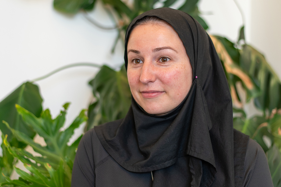 Portrait of a woman wearing a black hijab against a backdrop of large tropical houseplants.