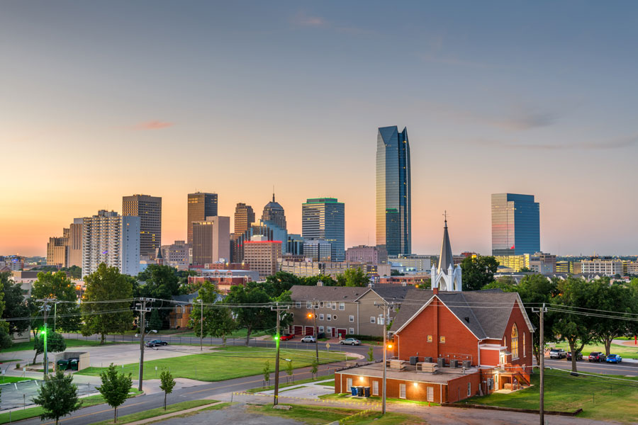 Oklahoma City skyline at dusk with a red brick church in the foreground and the Devon Energy Center tower rising above downtown.