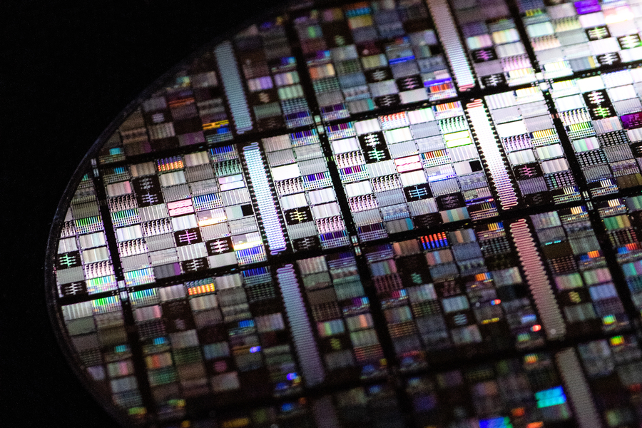 A close-up of a circular silicon wafer densely patterned with colorful superconducting qubit circuits, photographed against a black background.