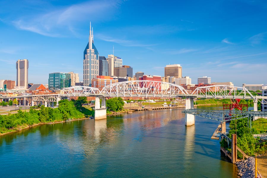 Nashville, Tennessee skyline along the Cumberland River, with the Shelby Street Pedestrian Bridge in the foreground and the AT&T Building rising above downtown on a clear summer day.