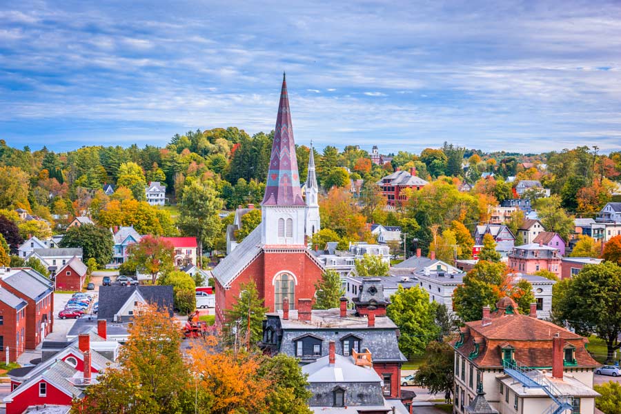 Aerial view of Montpelier, Vermont in peak fall foliage, centered on a red brick church with a distinctive patterned steeple amid a canopy of autumn color.