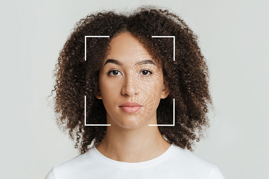 A portrait of a woman with curly hair against a gray background, with a white facial recognition grid overlay on her face.