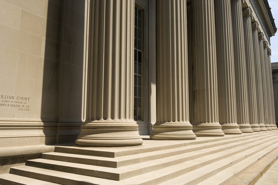 A low-angle view of a row of tall neoclassical stone columns and wide steps on the exterior of Killian Court at MIT.