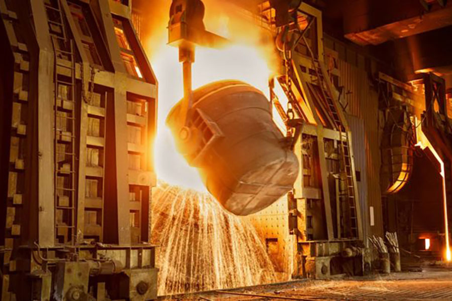A large ladle pours molten steel in a factory, sending bright sparks cascading across the industrial floor.