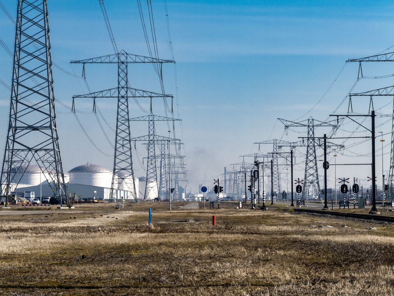Multiple high‑voltage transmission towers running alongside railway tracks across an open field.