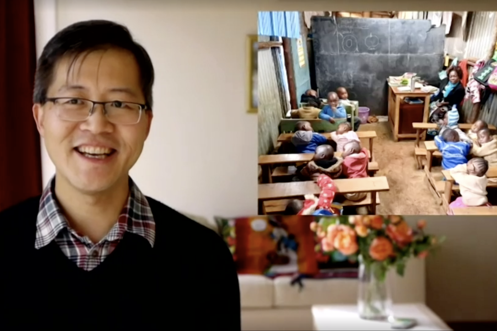 A video call screenshot showing a man smiling on the left beside a shared screen image of young children seated at desks in a modest classroom.