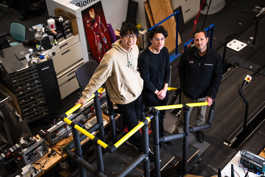 Three people standing on a testing platform inside a lab with equipment, cables, and railings.