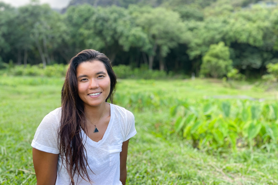 Portrait of an MIT researcher smiling outdoors in front of lush green taro fields and forested hills in Hawaii.
